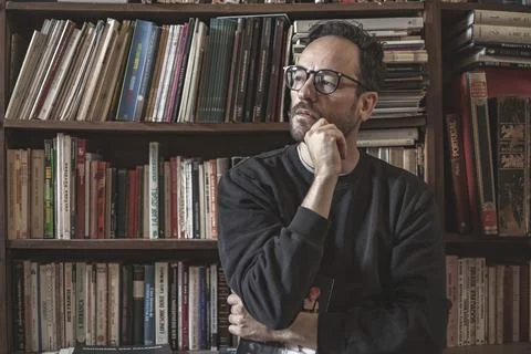 View of an handsome guy reading a book in a library alone wearing glasses, Li Stock Photos
