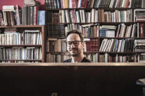 View of an handsome guy reading a book in a library alone wearing glasses, Li Stock Photos