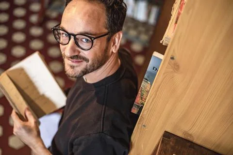 View of an handsome guy reading a book in a library alone wearing glasses, Li Stock Photos