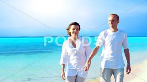 View of happy young couple walking on the beach, holding hands. Stock Photos