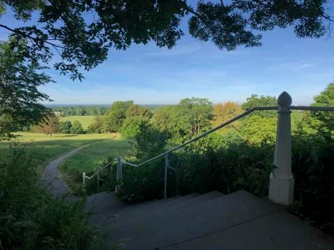 View from hill across fiels with path steps and railing, sunny day Stock Photos