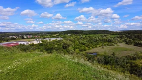 View from hill overlooking green fields and blue skies in summer Видео 340448262