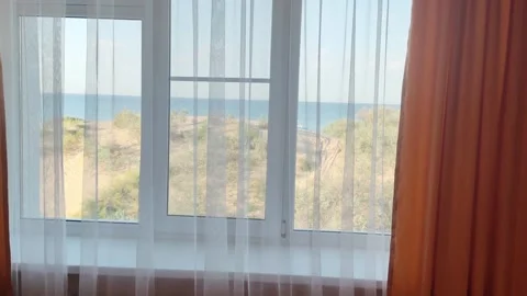 View from a hotel window with orange curtains to dunes with sand and the sea Stock-Footage 295603243