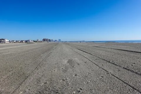 View up a huge empty beach with tire tracks towards several large buildings Stock Photos