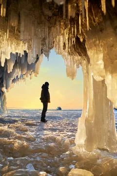 View from the ice cave with huge icicles on the frozen Lake Baikal at sunset. Stock Photos