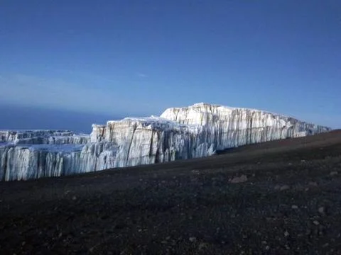 A view of an ice iceberg down a slope from dirt land. Cold winter landscape Stock Photos