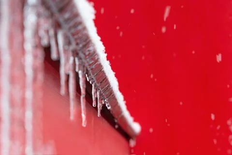 View of the icy windowsill with icicles on the background of the red wall of the Stock Photos