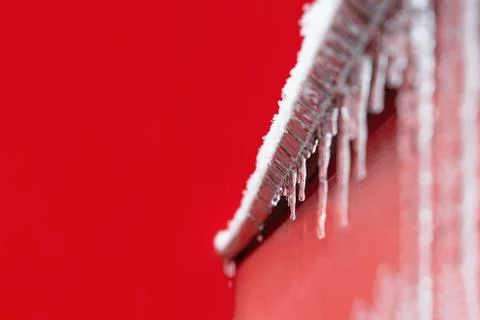 View of the icy windowsill with icicles on the background of the red wall of  Stock Photos