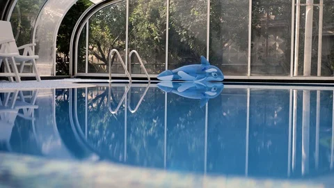 View of indoor pool with bright blue water on side lies an inflatable dolphin Stock Footage 120837874