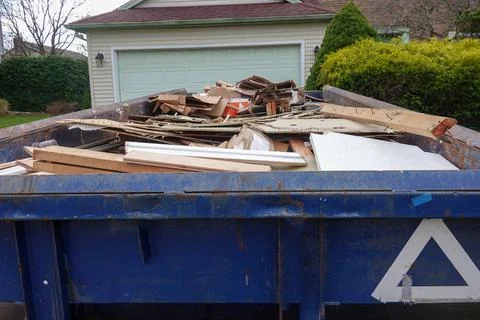 View inside a blue dumpster full of construction debris in front of a garage  Stock Photos