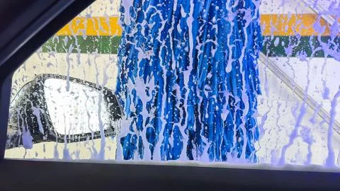 View from inside a car during a car wash with soap and brushes. Stock Photos