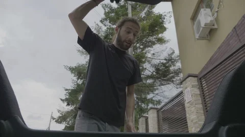 View from inside car of happy young man opening trunk and loading travel lugg Stock Footage 102440052