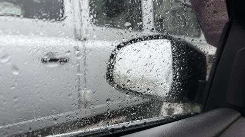 View from inside a car looking through a rain-covered window at a parked white Stock Photos