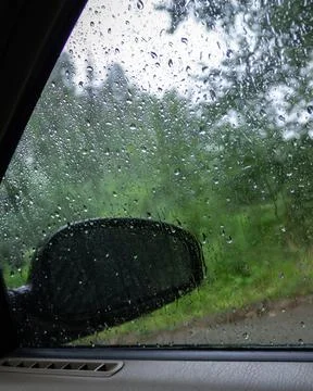 View from inside a car through a rain-covered window with visible side mirror Stock Photos