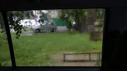 View from inside car through side window to yard with bench which it is raining Stock Footage 195213607