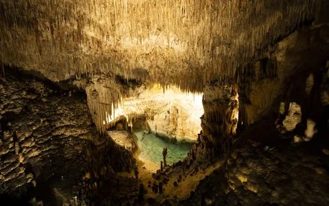 View inside of dark cave with stalactites and pool of water Фото