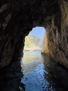 A view from inside a sea cave, looking out at the blue water and the rocky Stock Photos