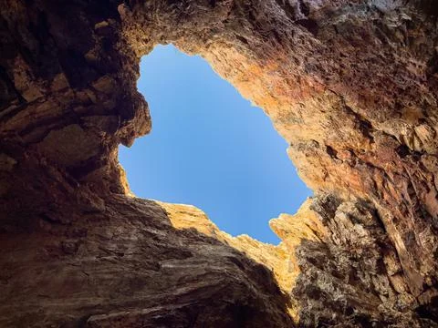 A view from inside a sea cave, looking out at the blue water and the rocky Stock Photos