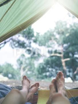 View from inside a tent at the forest and legs of two people emerge from tent Stock Photos