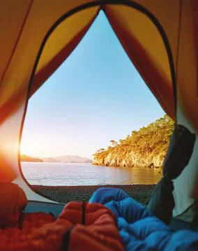 View from inside a tent at wild beach at sunrise and legs of two people in Stock Photos