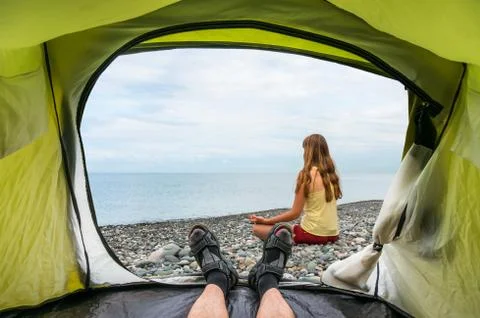 View from inside a tent on the young lady practicing yoga at seashore in summ Stock Photos