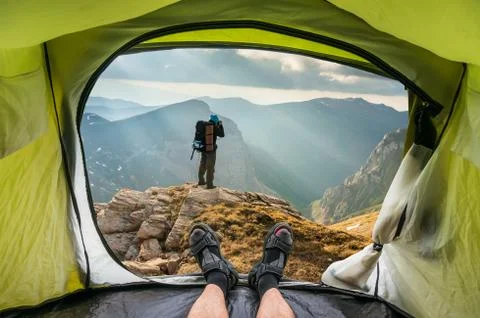 View from inside a tent on the young man on a rock and beautiful mountains in Stock Photos