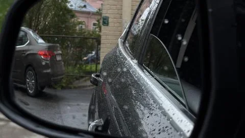 View from inside a vehicle through a wet side window showing a dark parked SUV Stock Photos