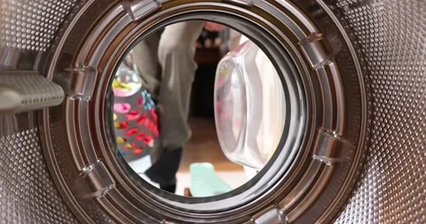 View from inside the washing machine drum. Young man is loading laundry in wa Stock Footage 152857385
