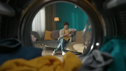 View from inside the washing machine, young man sitting on the couch in the room Stock Footage 247466106