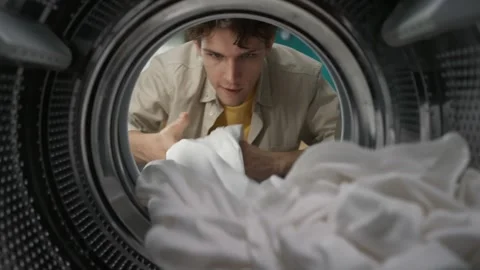 View from inside the washing machine, young man takes out the clean white sheet Video stock 247466943