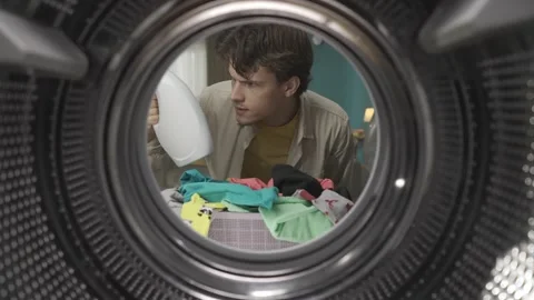 View from inside the washing machine, young man holding a bottle of fabric Stock Footage 247486589