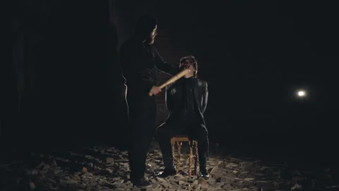 View of a kidnapper beating a tied man with strick in dark catacombs Stock Footage 99168772