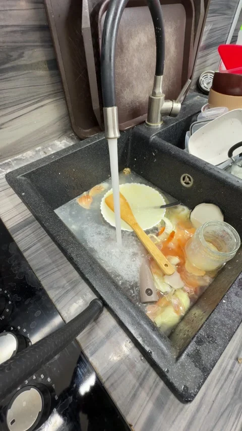View from a kitchen sink filled with dirty dishes and food scraps while water Video stock 321763967