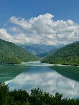 View of a lake between two lushy green hills with reflection in valley Stock Photos