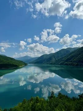 View of a lake between two lushy green hills with reflection of cloudy sky Stock Photos