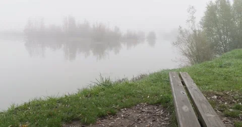 View of the lake shore over an empty wooden bench on a misty day Stock-Footage 220599132