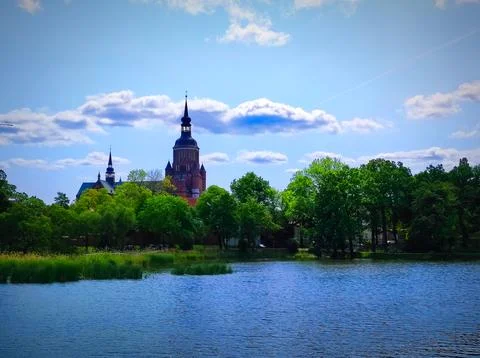 View of a lake surrounded by trees and a church in the background on a sunn.. Stock Photos