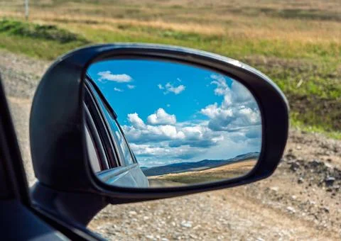 View of landscape reflected in side mirror while driving on gravel road Stock Photos