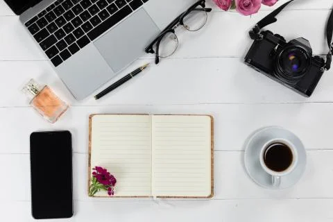 View of a laptop with a camera and a phone, perfume and notebook on white wood Stock Photos