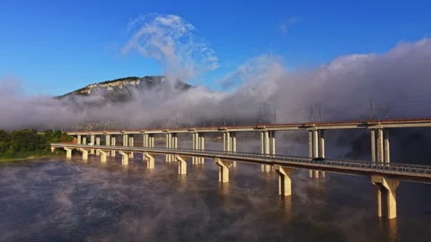 View of a large bridge over a river surrounded by fog and mountains on a clear Stock Footage 341105356