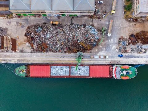 View of a large cargo ship loading materials at a dock near a pile of scrap.. Stock Photos