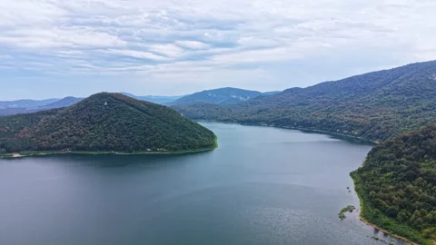 View of a large lake surrounded by green hills and trees under a cloudy sky Stock Footage 344792091