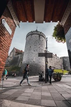 A view of a large stone castle seen from a narrow brick walkway. Stock Photos