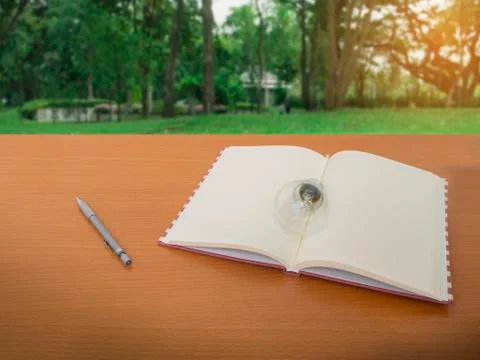 View of light bulb notebook and pencil on wooden table with green tree backgr Stock Photos
