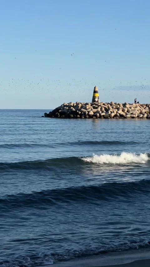View of lighthouse with birds flying from beach in Benalmadena, Spain. Vertical Stock Footage 240921354