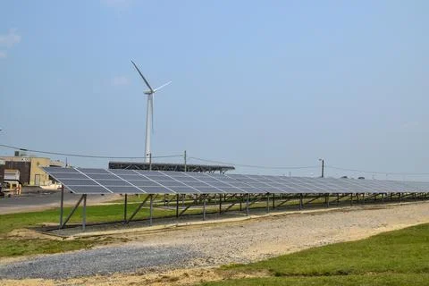 View of a long array of solar panels with an electric generating wind turbine Stock Photos
