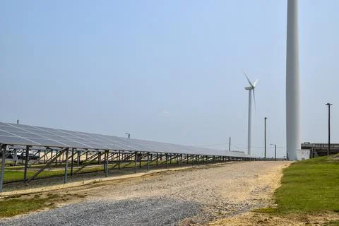 View of a long array of solar panels with an electric generating wind turbine Stock Photos