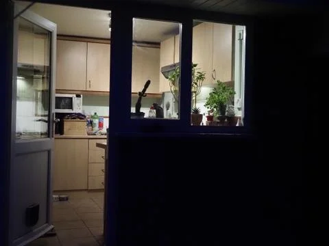 A view looking into a lit kitchen at night time from outside Stock Photos