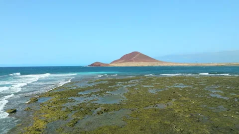View from a low drone flight passing over the waves, Montaña Roja in the horizon Stock Footage 202251095