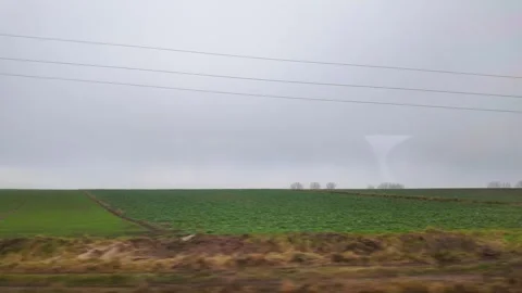 A view of lush green agricultural fields passing by a train window on a gray Stockbeeldmateriaal 345669666